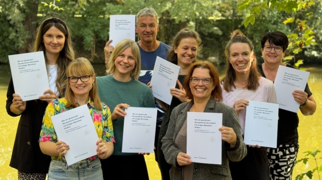 Das Team von Irrsinnig Menschlich e.V. hält den Jahresbericht 2023 hoch.